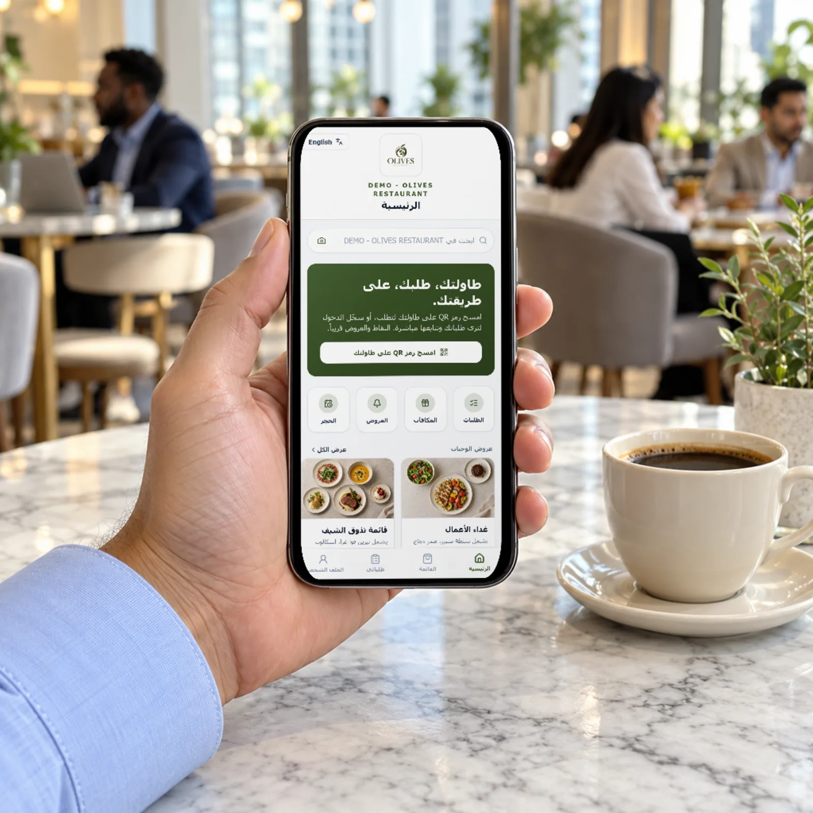 A hand holding a phone with a restaurant ordering app shown in Arabic, at a café table